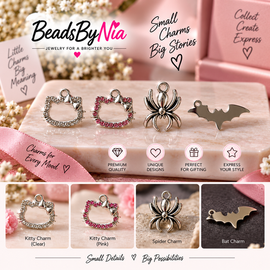 A promotional collage for jewelry charms by BeadsByNia, showing four metal charm designs: a clear rhinestone cat head charm, a pink rhinestone cat head charm, a silver spider charm, and a silver bat charm. The charms are displayed on a pink marble slab with pink packaging and decorative flowers in the background.